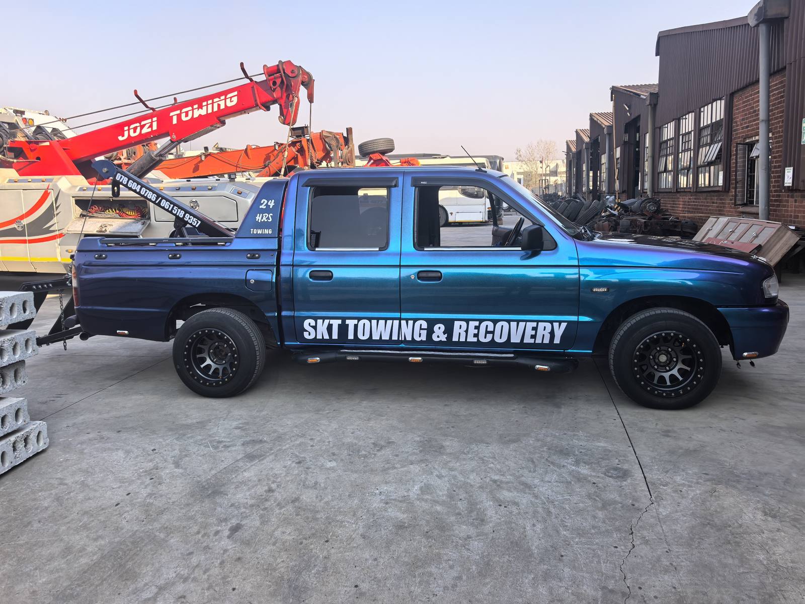 A side view of a blue pickup with white SKT Towing and Recovery lettering.